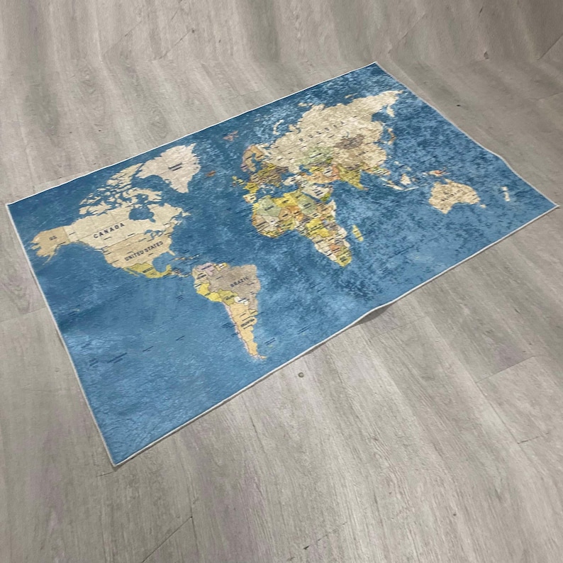 May include: A rectangular rug featuring a world map design. The rug has a blue background with a detailed map in shades of beige, yellow, and green. The map includes country names and borders, suitable for a living room or study.