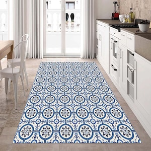 May include: A rectangular kitchen rug with a repeating pattern of blue and white floral and geometric designs. The rug is placed in front of a white kitchen cabinet and a white door with a view of the outside.