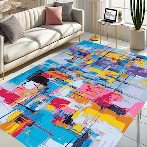 May include: A large, rectangular area rug with an abstract design. The rug features a vibrant mix of colors, including blue, pink, yellow, and purple, with black lines overlaying the design. The rug is placed on a white floor in a living room setting.