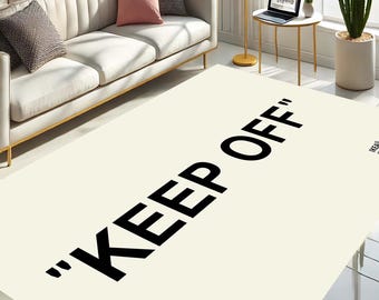 May include: A white rug with the text "KEEP OFF" in black lettering. The rug is on a hardwood floor in a living room setting.