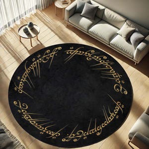 Peut inclure: Un tapis rond noir avec des lettres dorées qui disent "Un anneau pour les gouverner tous, Un anneau pour les trouver, Un anneau pour les amener tous et dans les ténèbres les lier."