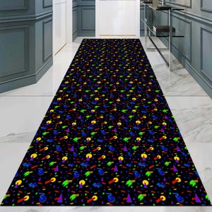 May include: A long, rectangular black hallway runner rug with a repeating pattern of colourful geometric shapes, including triangles, circles, and curved lines in red, yellow, green, and purple. The rug is placed on a white tiled floor.