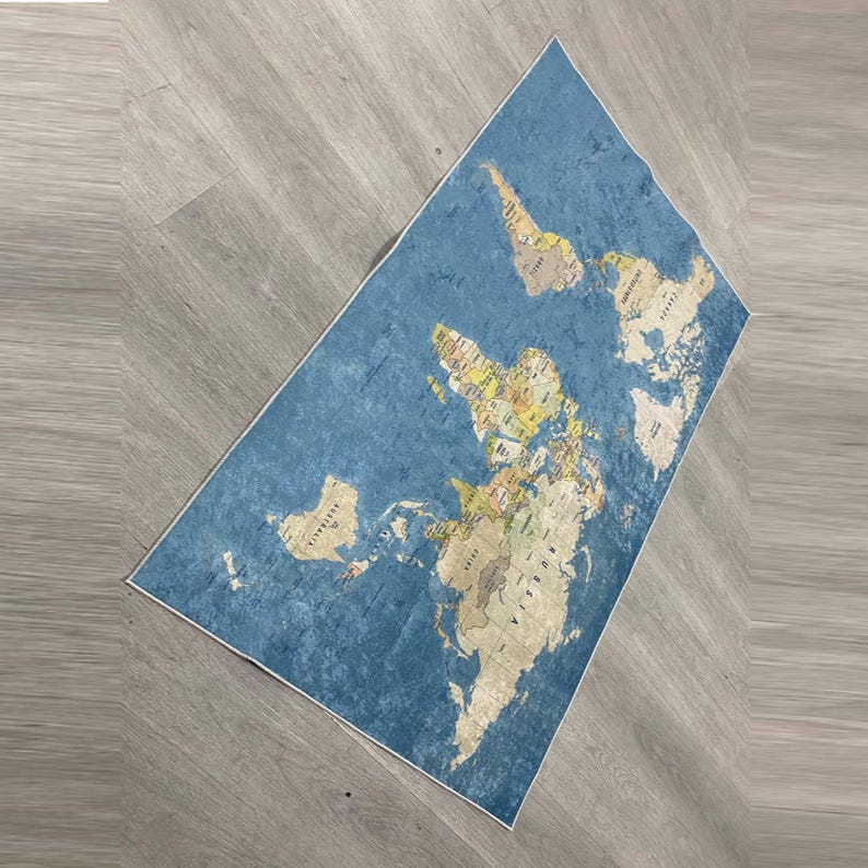 May include: A rectangular blue rug with a world map design. The map features continents in beige and countries in various colors. The rug is placed on a light gray wooden floor.