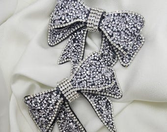 May include: Two black fabric bows covered in sparkling silver rhinestones. The bows are layered on top of each other.