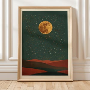 May include: A framed art print featuring a celestial landscape. The artwork depicts a large, golden moon and numerous stars against a dark teal sky. Below, there are layered red and brown hills. The print is encased in a light wood frame.