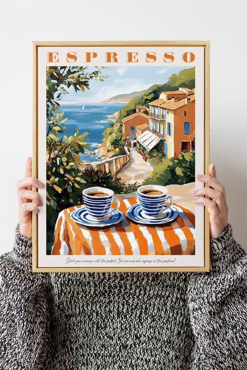 May include: A framed poster with a painting of a coastal town in Italy. The poster has the word "ESPRESSO" in orange letters at the top. The painting shows a view of the town from a cafe table with two cups of espresso on the table. The text at the bottom of the poster reads "Start your morning with the perfect Italian moment - espresso in the sunshine!"