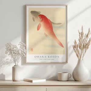 K&ouml;nnte beinhalten: Ein Vintage-Poster mit einem japanischen Gem&auml;lde von zwei Karpfen, einem roten und einem grauen, die in einem Teich schwimmen. Das Poster tr&auml;gt den Titel "Ohara Koson Zwei Karpfen (1890-1939)" und hat ein rotes Siegel in der oberen rechten Ecke.