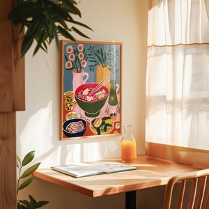 May include: A framed art print depicting a colorful still life of a ramen bowl, side dishes, and drinks. The artwork features a green bowl of ramen with chopsticks, a bottle, and a glass pitcher of orange juice on a wooden table.