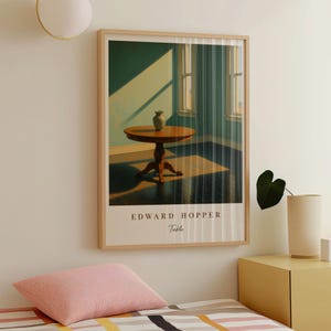 Puede incluir: Impresión artística enmarcada de una pintura de Edward Hopper titulada "Table". La obra representa una mesa redonda de madera con un jarrón, en una habitación con una ventana. La impresión está en un marco de madera clara.
