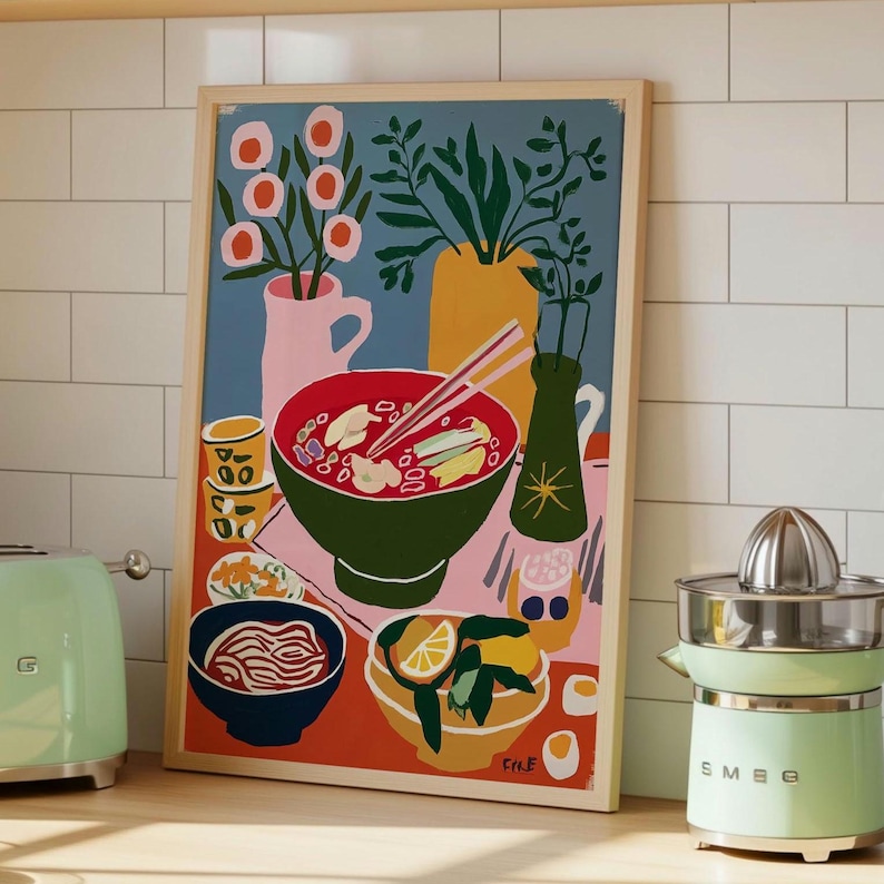 May include: A framed art print depicts a still life with a bowl of ramen, chopsticks, and various vases. The artwork features a green bowl of ramen with red broth, a pink vase with flowers, and a yellow vase with green leaves. A green juicer and a toaster are on the counter.