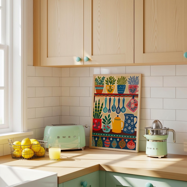 May include: A kitchen scene featuring a mint green toaster and juicer, a wire basket of lemons, and a framed print with colorful plant and kitchen utensil illustrations. The word "SMEG" is visible on the toaster. The kitchen has light wood cabinets and white subway tile.