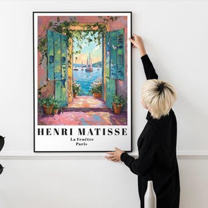 Peut inclure: Une estampe encadr&eacute;e d'une peinture d'Henri Matisse intitul&eacute;e "La Fen&ecirc;tre, Paris". La peinture repr&eacute;sente une vue color&eacute;e d'une fen&ecirc;tre avec des volets ouverts donnant sur un paysage maritime avec des voiliers.