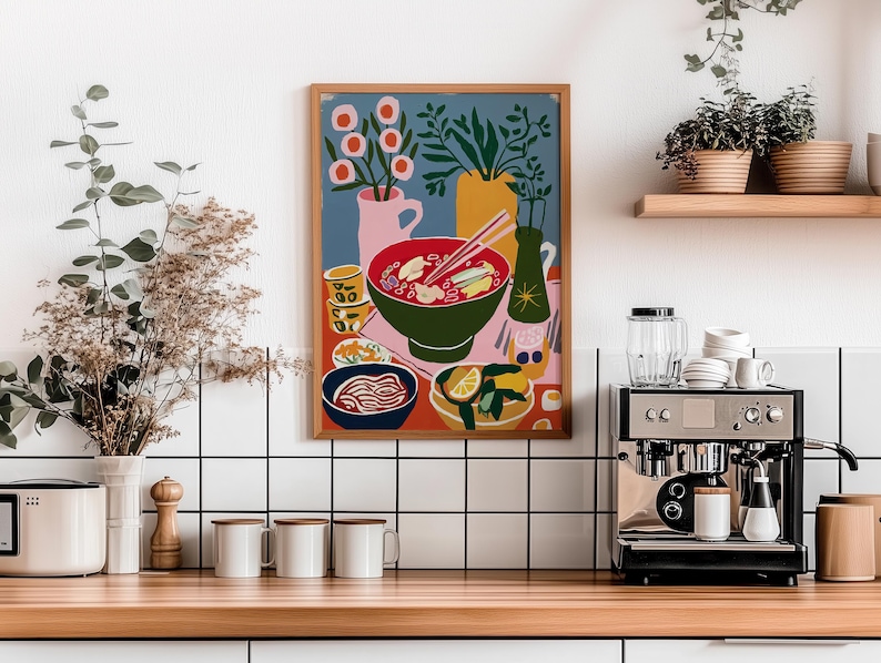 May include: A framed art print depicting a colorful still life of a meal, including a bowl of soup with chopsticks, a side of noodles, and a plate with lemon slices. The artwork is set against a blue background with pink and yellow accents.