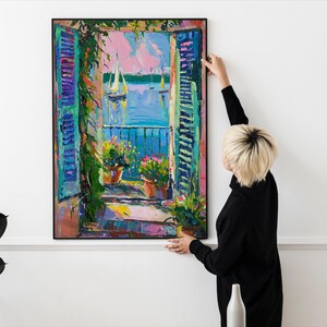 May include: A colorful painting of a window with open shutters overlooking a blue body of water with sailboats. The window is framed in black and the painting is hanging on a white wall.