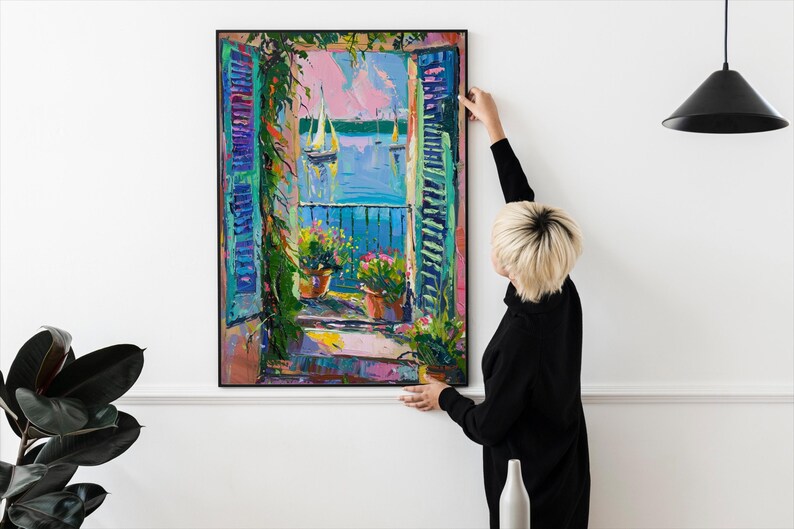 May include: A colorful painting of a window with open shutters overlooking a blue body of water with sailboats. The window is framed in black and the painting is hanging on a white wall.