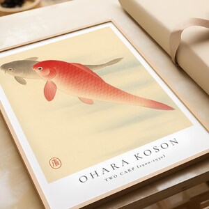 K&ouml;nnte beinhalten: Ein gerahmter Druck eines japanischen Gem&auml;ldes, das zwei Karpfen zeigt, einen roten und einen grauen, die in einem hellblauen Teich schwimmen. Der Name des K&uuml;nstlers, "Ohara Koson", und der Titel, "Zwei Karpfen (1900-1930)", sind unter dem Bild gedruckt.