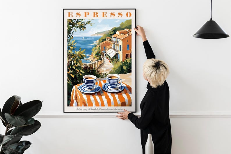 May include: A framed poster with a colorful illustration of a seaside town with two cups of coffee on a striped table. The poster has the word "ESPRESSO" in large letters at the top.