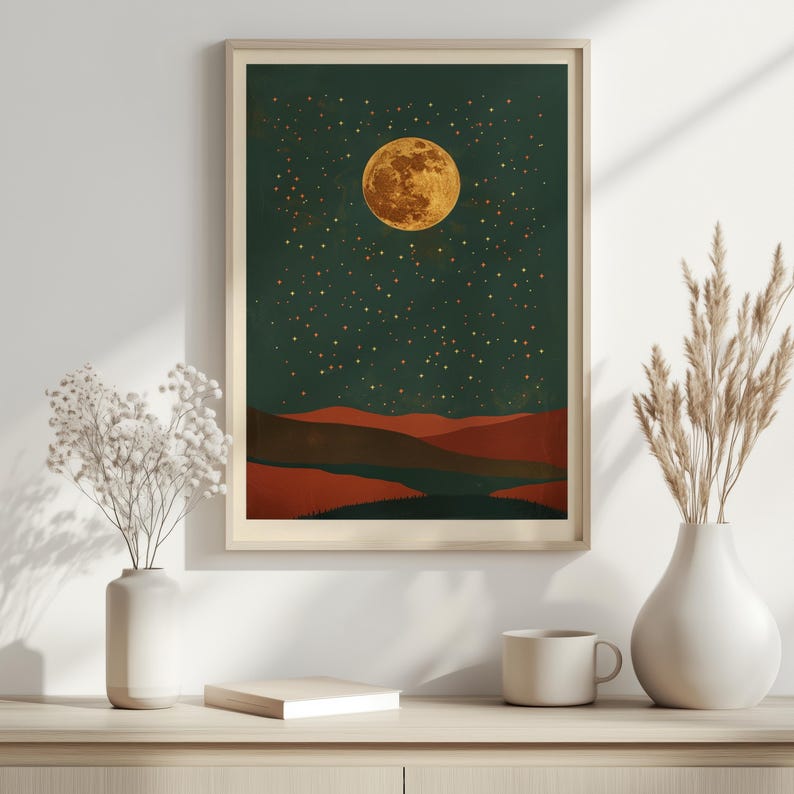 May include: Framed art print featuring a full golden moon and a starry night sky over a landscape of red and brown hills. The artwork is in a wooden frame and evokes a sense of tranquility.