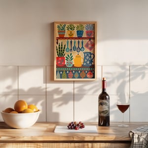 May include: A framed kitchen-themed art print featuring colorful potted plants, utensils, and a teapot. A bottle of red wine, a glass of wine, a bowl of oranges, and a bunch of grapes are on a wooden countertop.