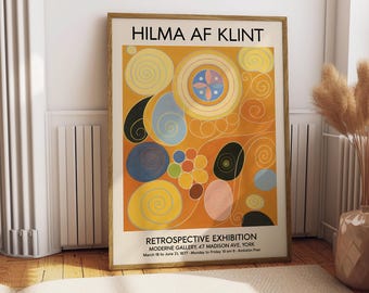 May include: A framed print of a Hilma af Klint abstract artwork. The piece features a warm orange backdrop with circular and organic shapes in yellow, blue, black, and pink. The print includes the text "HILMA AF KLINT" and details of a retrospective exhibition at the Moderne Gallery.