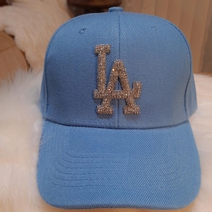 May include: A light blue baseball cap with a rhinestone "LA" logo.
