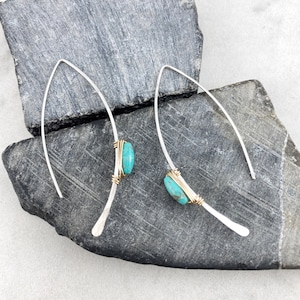 May include: A pair of silver earrings with turquoise stones set in gold wire. The earrings are long and thin, with a simple design.