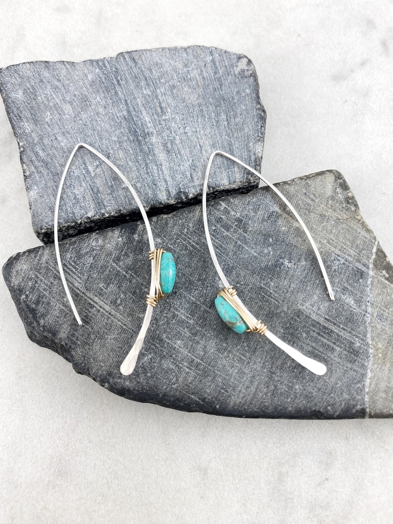 May include: A pair of silver earrings with turquoise stones set in gold wire. The earrings are long and thin, with a simple design.