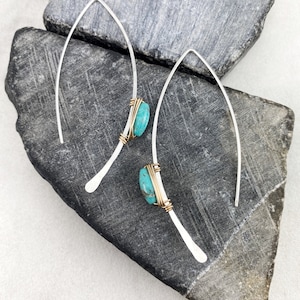 May include: A pair of silver earrings with turquoise stones wrapped in gold wire. The earrings are long and dangle.