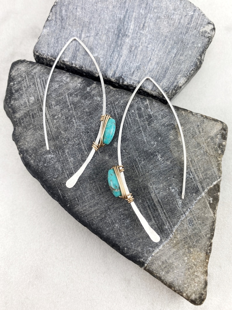May include: A pair of silver earrings with turquoise stones wrapped in gold wire. The earrings are long and dangle.