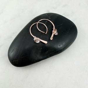May include: A pair of rose gold hoop earrings with clear quartz crystals. The earrings are handmade and feature a delicate wire design.