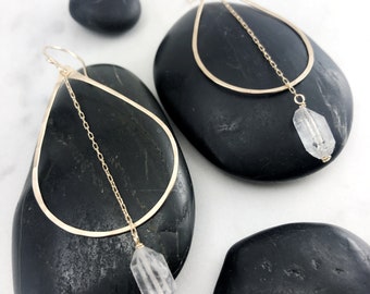 May include: Gold teardrop earrings with a delicate chain and a clear quartz crystal pendant.