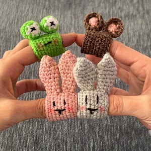Könnte beinhalten: Vier Fingerpuppen, zwei rosa Kaninchen, ein grüner Frosch und eine braune Maus. Die Puppen sind gehäkelt und haben gestickte Gesichter.