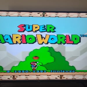 May include: A screenshot of the Super Mario World video game for the Super Nintendo Entertainment System. The title screen shows the game's logo, "Super Mario World", with a green, blue, yellow, and red color scheme. The text "1990, 1991 Nintendo" is displayed at the bottom of the screen.