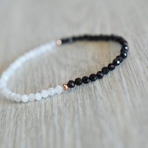May include: A black and white beaded bracelet with a rose gold accent. The bracelet is made with small, round beads and is approximately 7 inches in length.