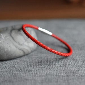 Könnte beinhalten: Ein rotes geflochtenes Lederarmband mit einem silbernen Verschluss.