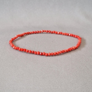 Könnte beinhalten: Ein zartes Armband aus roten Perlen. Das Armband besteht aus kleinen, facettierten Perlen, die eine durchgehende Schleife bilden. Die Perlen sind leuchtend rot, und das Armband wird auf einem neutralen grauen Hintergrund präsentiert.