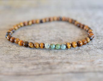 May include: A brown and gold beaded bracelet with a row of turquoise beads in the center.