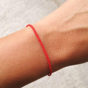 Könnte beinhalten: Ein rotes geflochtenes Armband, das an einem Handgelenk getragen wird.