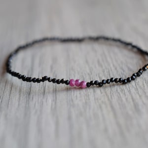 Op de afbeelding: Een delicate armband gemaakt met zwarte kralen en drie roze kralen in het midden.