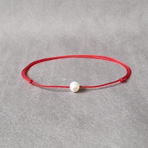 Op de afbeelding: Een eenvoudige rode armband met een enkele witte parelbedel.