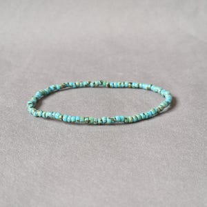 Pode incluir: Um bracelete de contas azul turquesa com um design simples. O bracelete é feito de pequenas contas redondas que são enfiadas em um cordão fino.