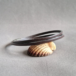 Op de afbeelding: Een bruin leren armband met een zilveren sluiting. De armband is gelaagd en heeft een eenvoudig ontwerp.