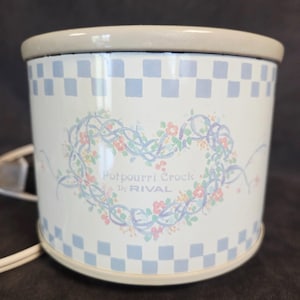May include: A white potpourri crock by Rival with a light blue and white checkered pattern around the top and bottom. The crock features a floral heart design with the words "Potpourri Crock" in the center.