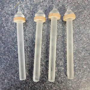 May include: Four identical glass stirrers arranged vertically. Each stirrer features a long, frosted cylindrical stem, a smooth light-colored wooden ring accent near the top, and a clear, pointed, teardrop-shaped glass finial at the very tip.