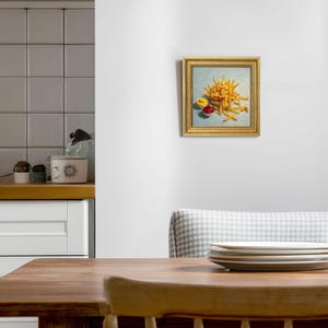 May include: A framed painting depicting a pile of golden-brown chips, alongside small dishes of yellow mustard and red ketchup. The artwork, in a gold frame, hangs on a white wall. The image is a still life of fast food.