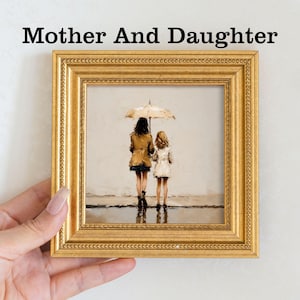 Pu&ograve; includere: Un'opera d'arte incorniciata con la scritta "Mother And Daughter". Il dipinto raffigura una madre e una figlia che camminano sotto un ombrello. La cornice &egrave; dorata e rettangolare.