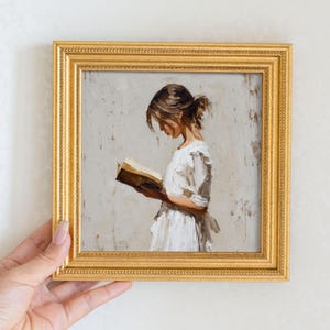 Pu&ograve; includere: Dipinto incorniciato di una persona che legge un libro. L'opera raffigura una persona con un vestito bianco, assorta nella lettura. La cornice &egrave; dorata e il dipinto ha una tavolozza di colori caldi e tenui.