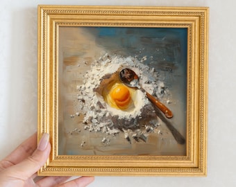 May include: A framed oil painting depicts a raw egg yolk in a nest of flour, with a spoon resting beside it. The painting has a gold frame and a neutral color palette, with shades of yellow, brown, and white.