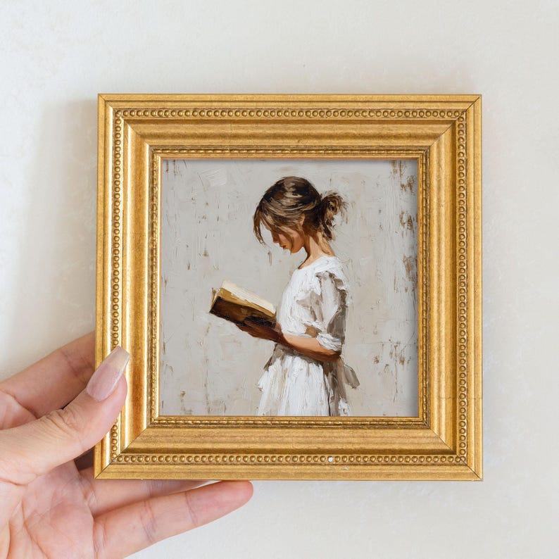 Pu&ograve; includere: Un'opera d'arte incorniciata raffigurante una donna che legge un libro. Il dipinto &egrave; in una cornice dorata. La donna indossa un vestito bianco. L'opera d'arte ha uno sfondo neutro.
