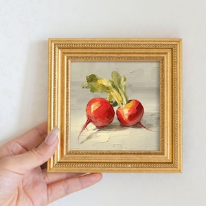 Könnte beinhalten: Gerahmtes Ölgemälde mit zwei roten Radieschen mit grünen und gelben Blättern. Das Gemälde befindet sich in einem goldenen Rahmen. Die Radieschen sind realistisch gemalt.